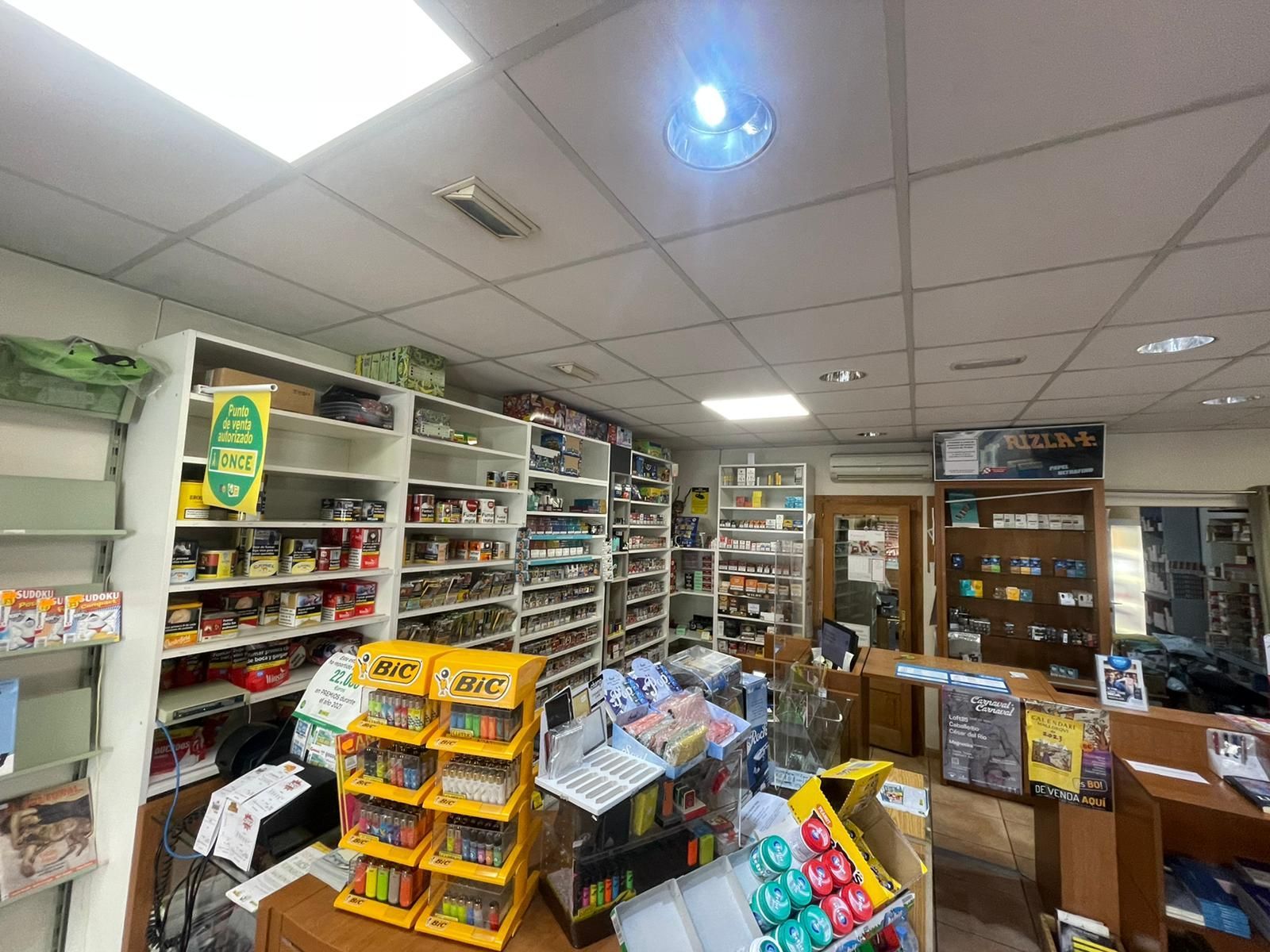 Fotografía interior de una tienda desordenada. Estantes llenos de productos, varios expositores y una lámpara en el techo.