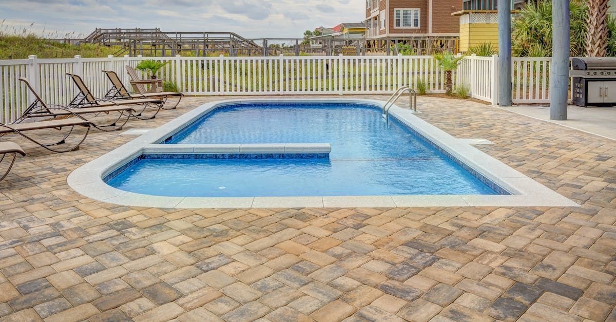 A large swimming pool surrounded by chairs and a brick patio.