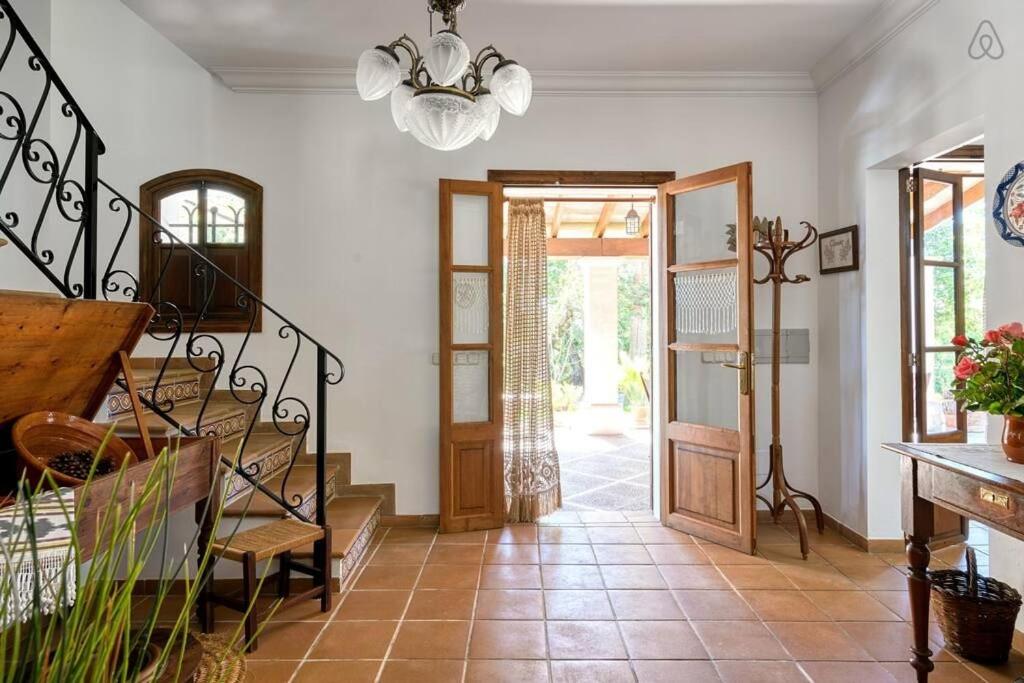 Entrada de azulejos con puertas de madera que dan a un patio soleado. Escalera con barandilla de hierro forjado a la izquierda.