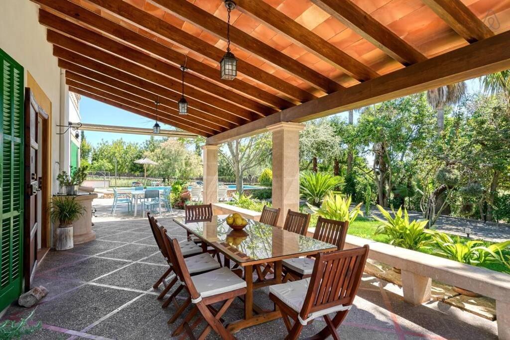 Comedor exterior cubierto con mesa larga de madera, sillas y vista al jardín.