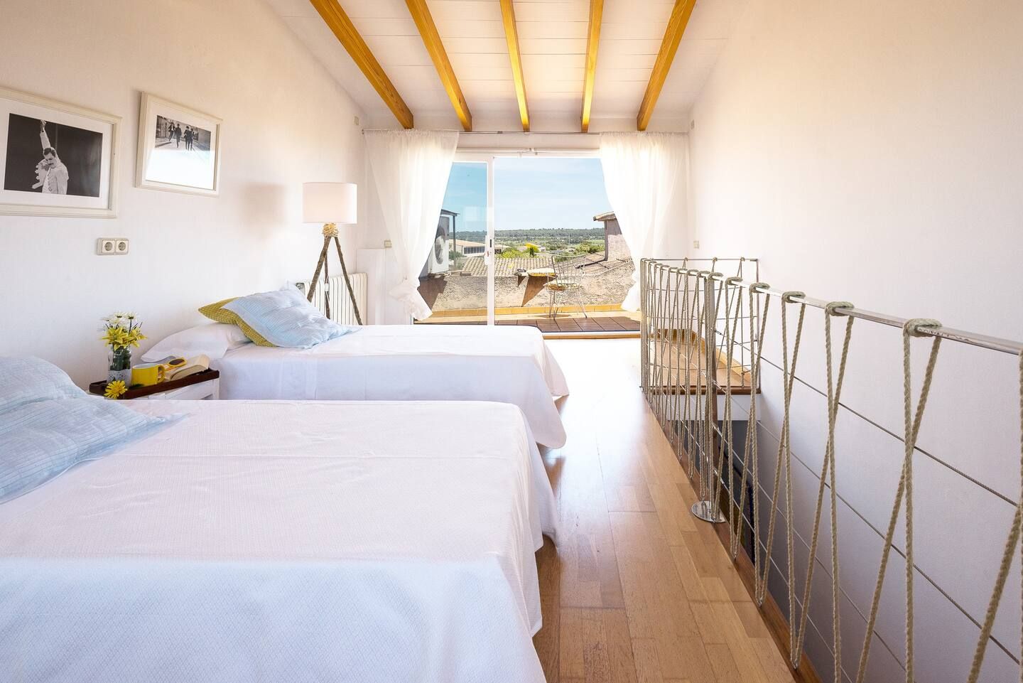 Dormitorio con dos camas blancas, vista al balcón y techo con vigas de madera.