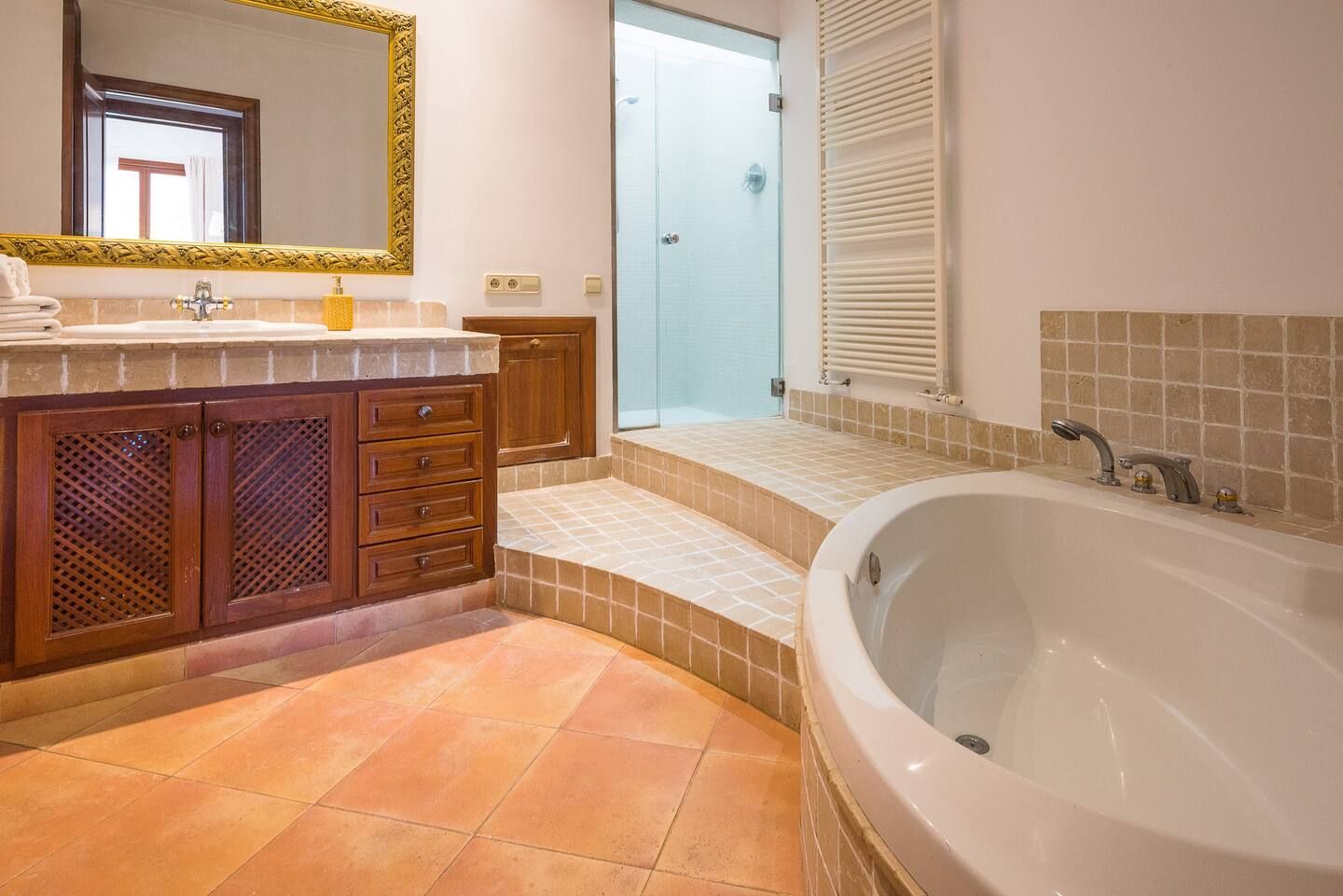 Baño con bañera grande ovalada, escalones de baldosas y ducha separada con mampara de cristal.