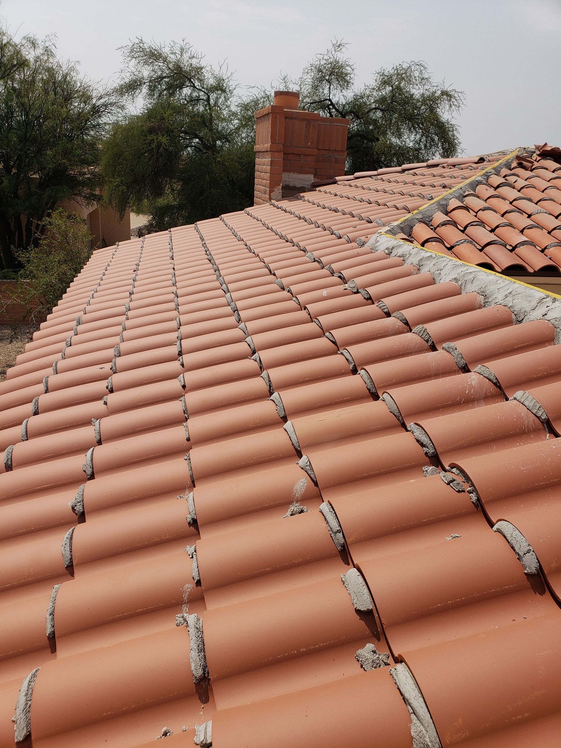 Terracotta tiled roof with a brick chimney, viewed from above with trees in the background