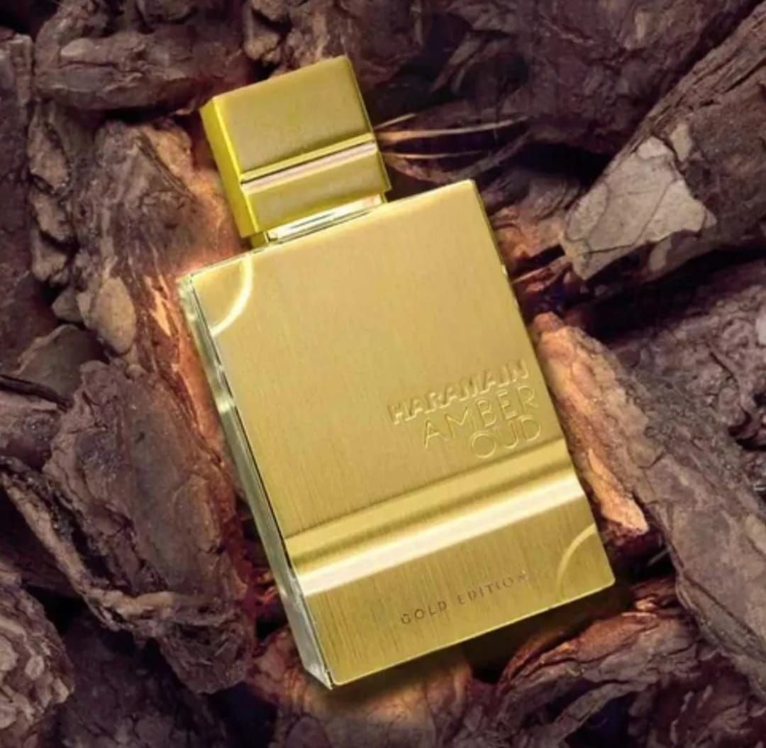 Frasco de perfume dorado sobre fondo marrón texturizado. El frasco tiene tapón, texto y detalles dorados.