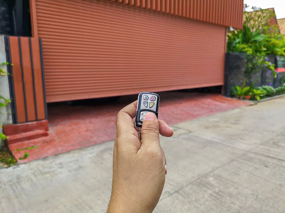 A Person Is Holding A Remote Control In Front Of A Garage Door — Upright Garage Doors In Chipping Norton, NSW