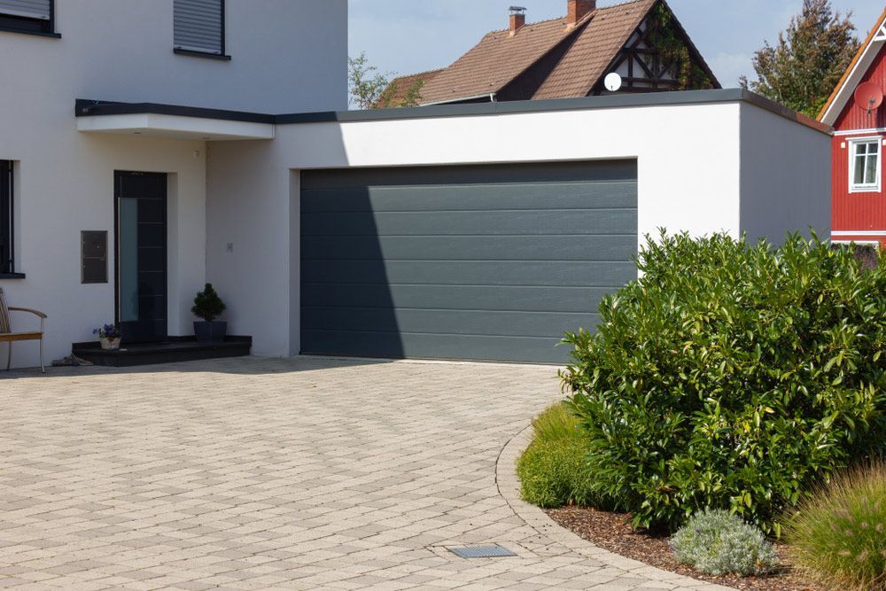 A White House With A Gray Garage Door And A Red House In The Background — Upright Garage Doors In Chipping Norton, NSW