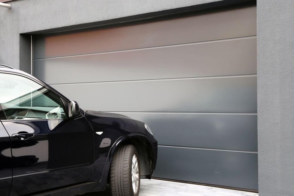 A Black Car Is Parked In Front Of A Garage Door — Upright Garage Doors In Chipping Norton, NSW