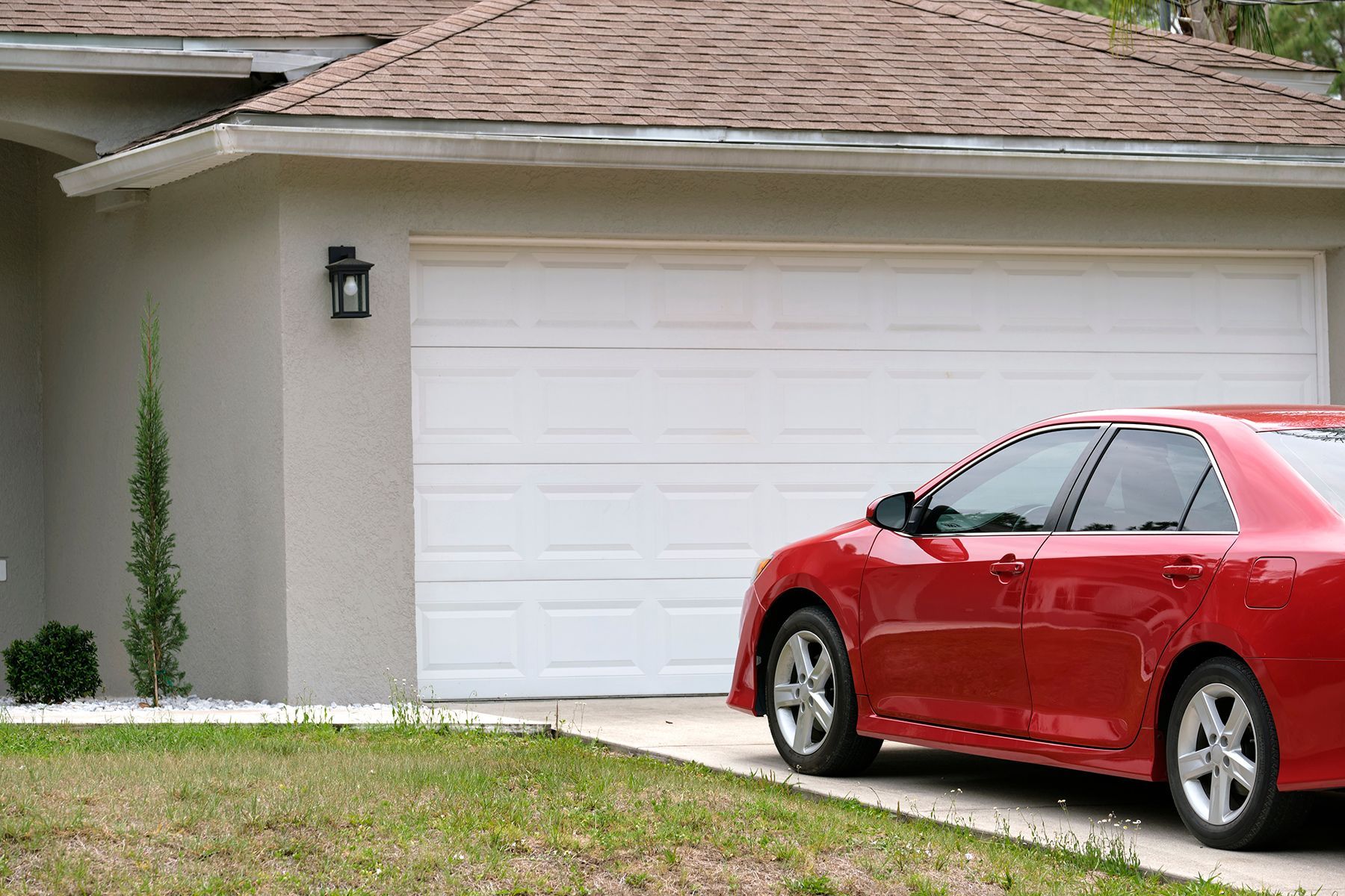A Red Car Is Parked In Front Of A White Garage Door — Upright Garage Doors In Chipping Norton, NSW