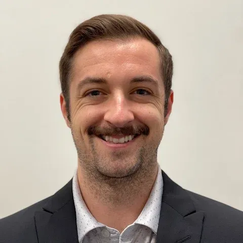 Smiling man in a dark blazer and white shirt against a plain light background