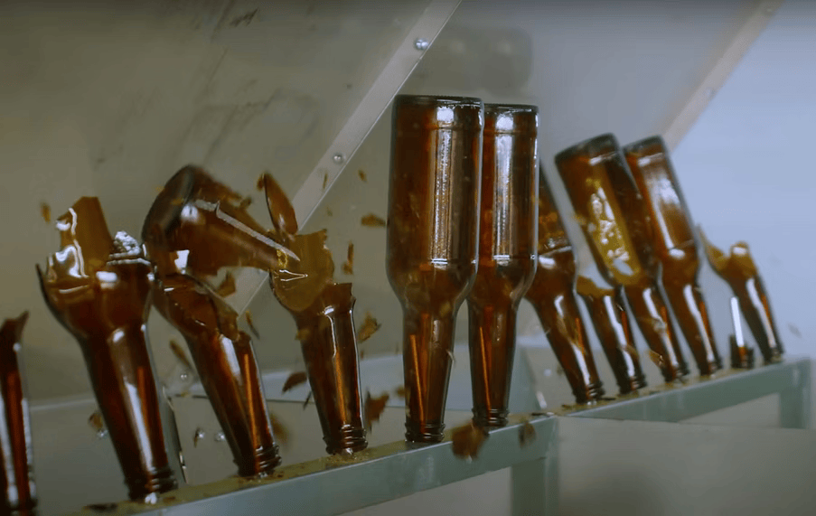 Broken brown glass beer bottles in a slanted rack, with shards scattered.