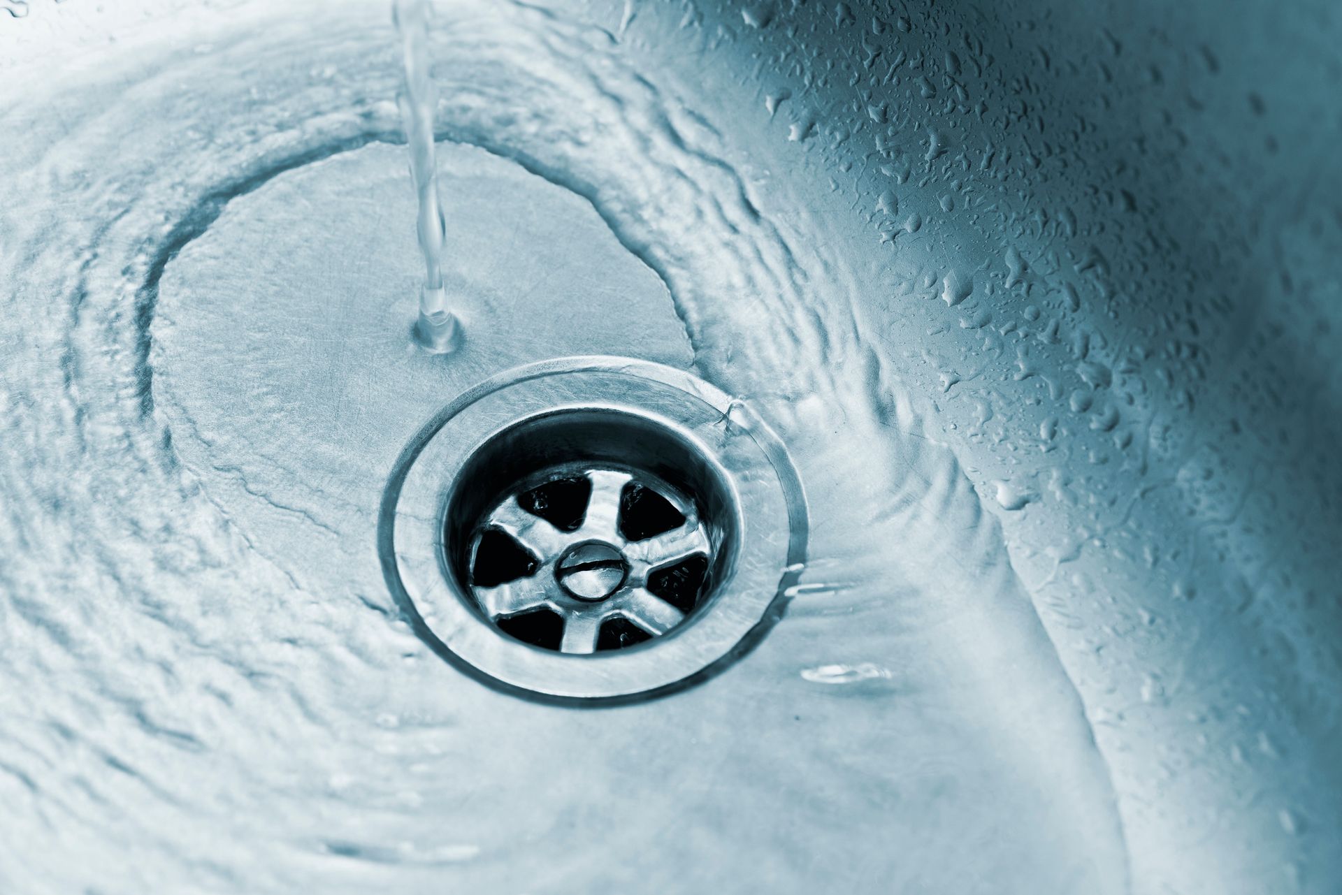 Close-up of a drain with water running from a kitchen faucet.