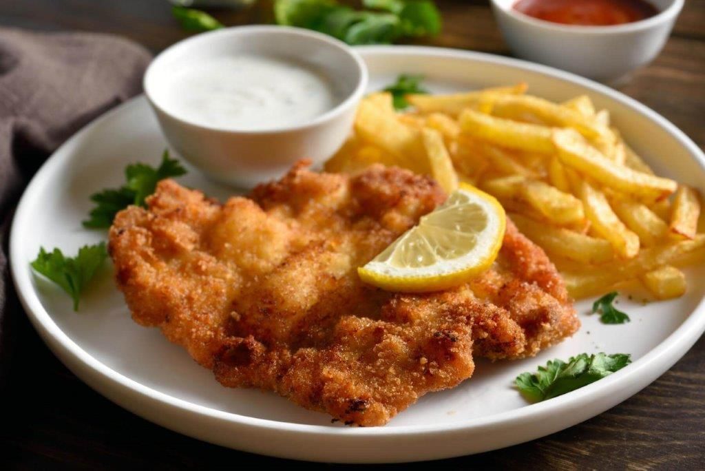 Un piatto bianco con sopra una cotoletta alla milanese e patatine fritte.