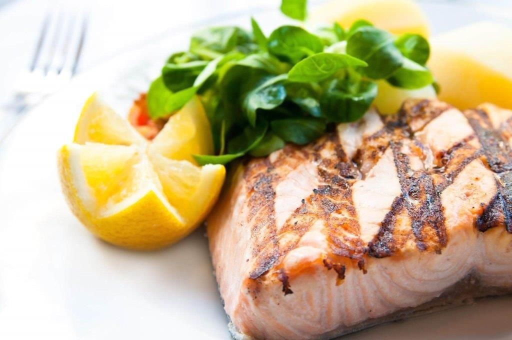 Un piatto bianco con sopra un pezzo di salmone, patate e fette di limone.