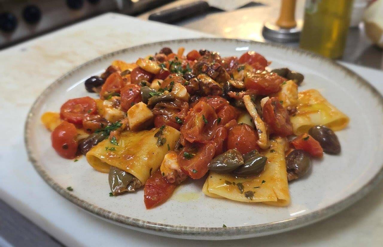 Un piatto bianco condito con pasta, pomodori e olive