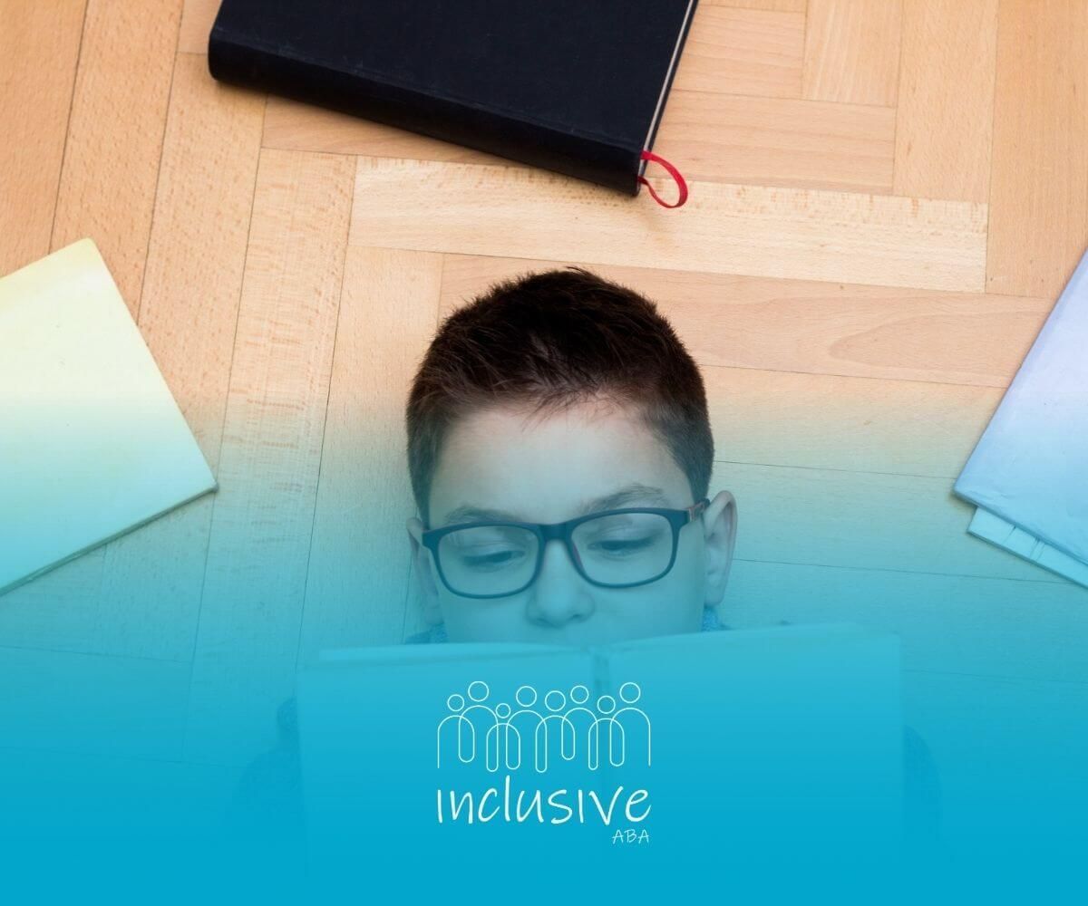 Boy with autism lying on the floor reading a book surrounded by other books.