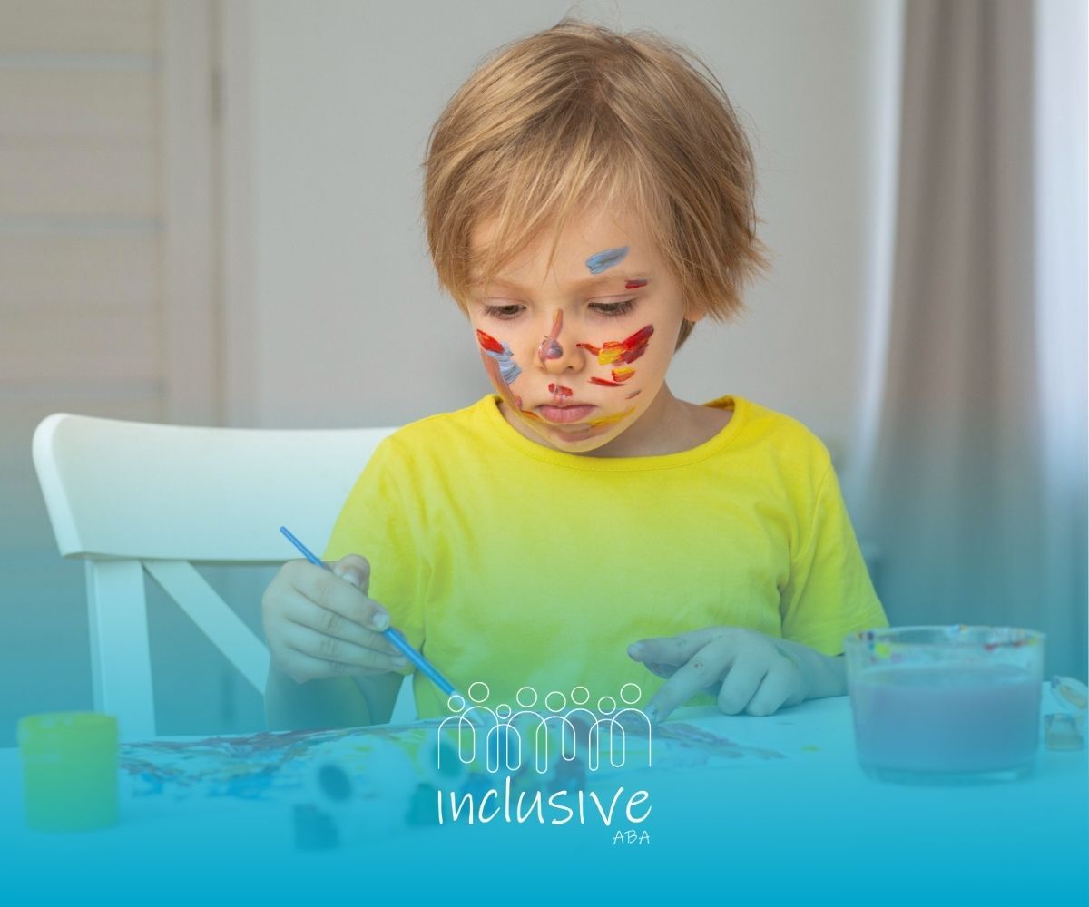 A little boy with paint on his face is sitting at a table.