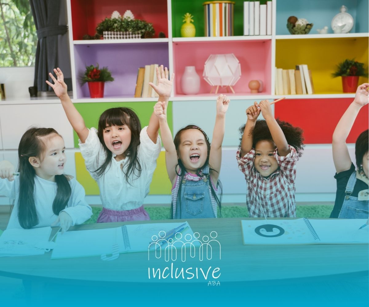 A group of children are sitting at a table with their hands in the air.