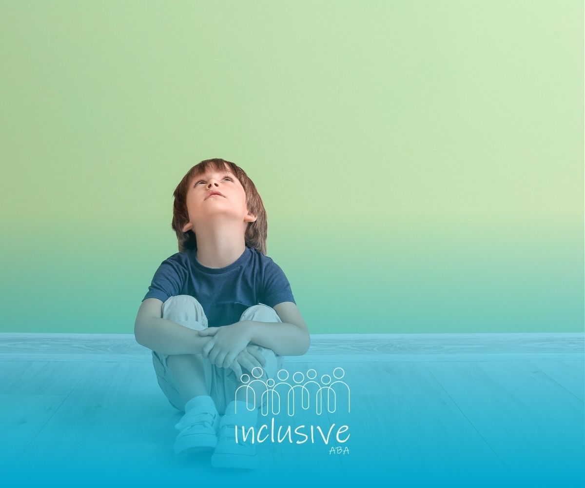 A little boy is sitting on the floor in front of a green wall looking up.