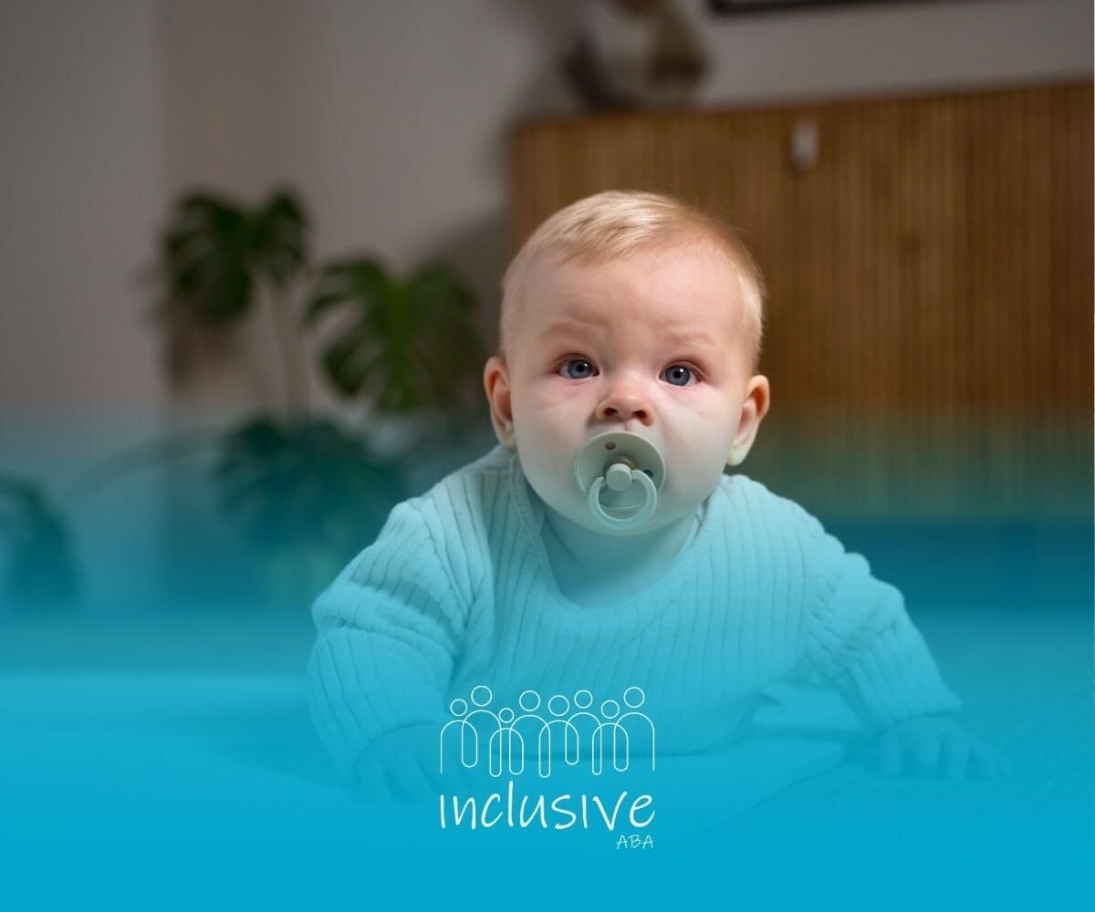 A baby with autism is sitting on the floor with a pacifier in his mouth.