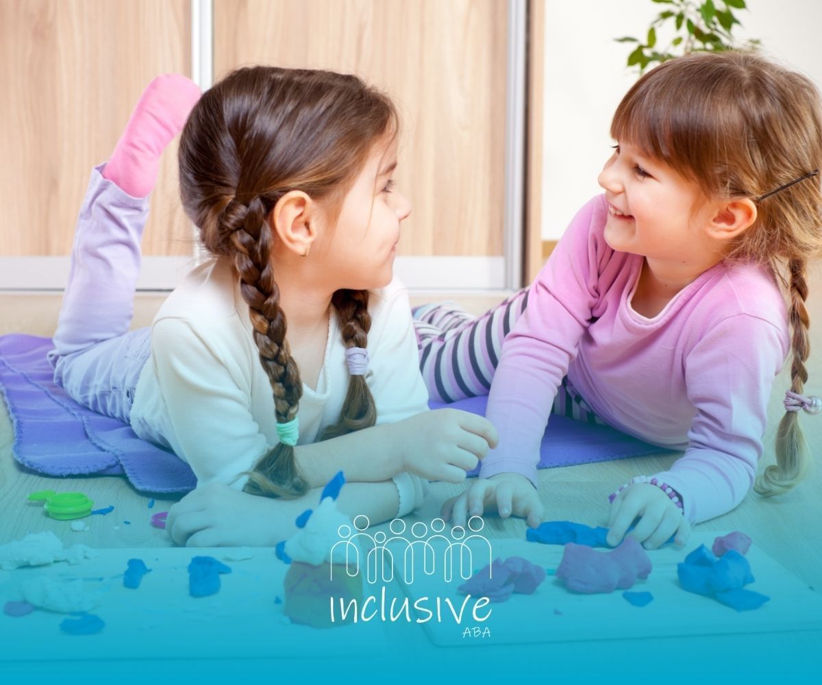 Two children lying on a mat, smiling at each other in a bright playroom