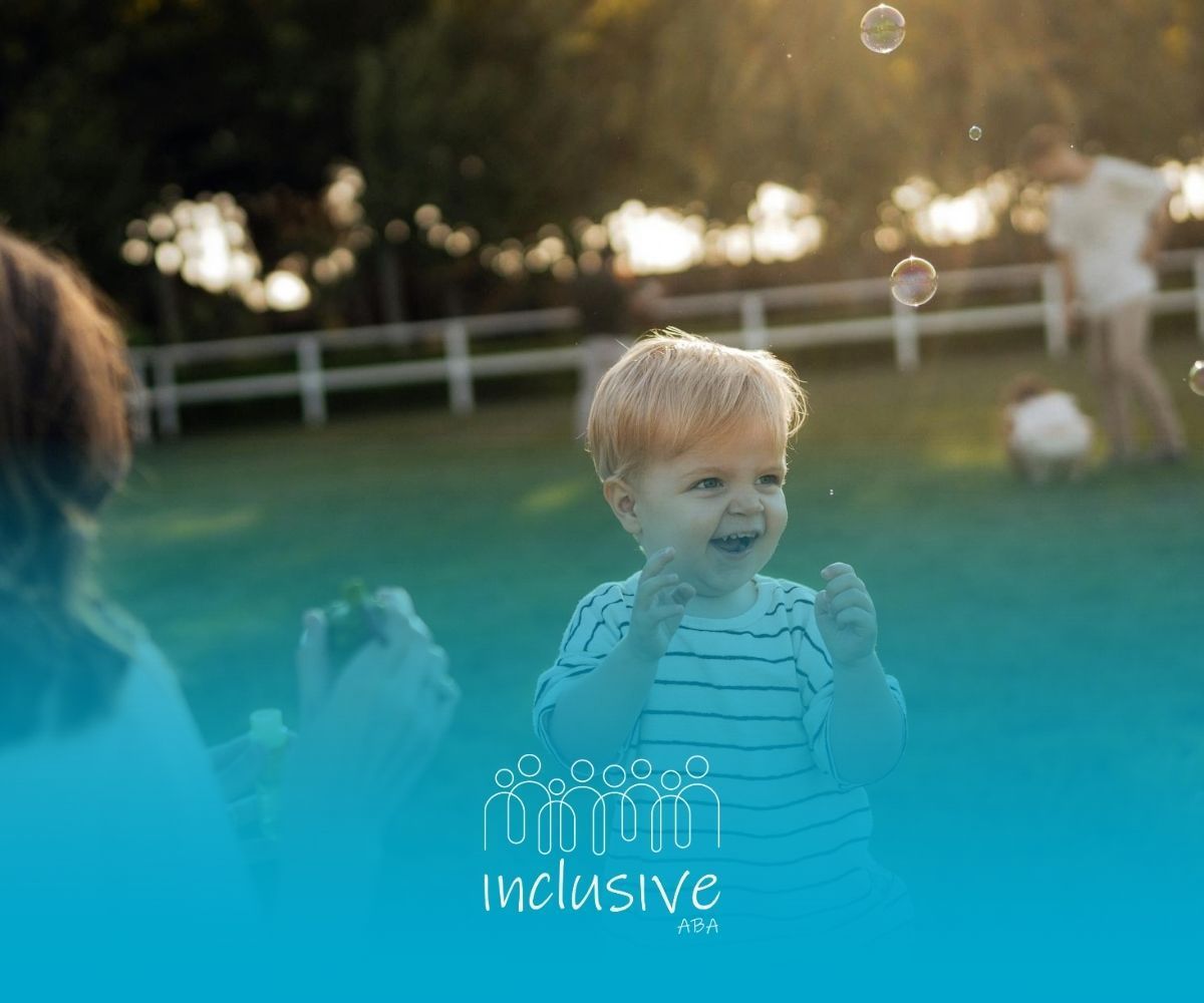 An autistic toddler laughing while playing with bubbles on grass during ABA therapy in Nebraska.