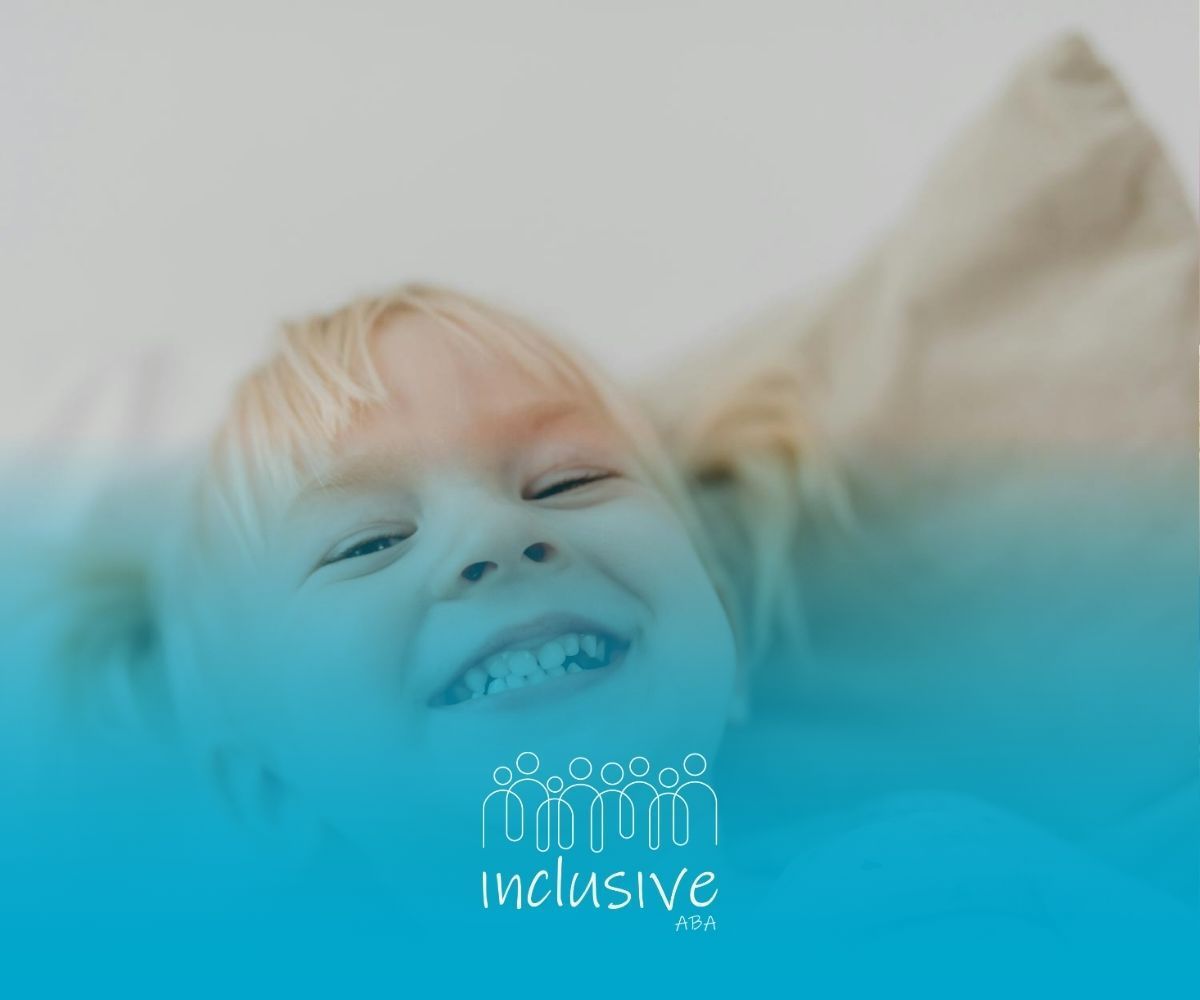 Blonde autistic toddler smiling while lying on a pillow during ABA therapy session in Nevada.