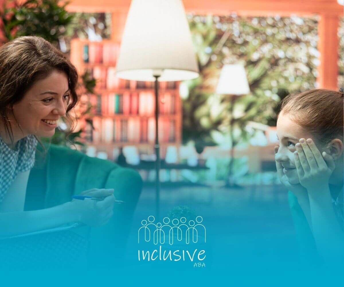 A BCBA is sitting at a table talking to a young girl during ABA therapy.