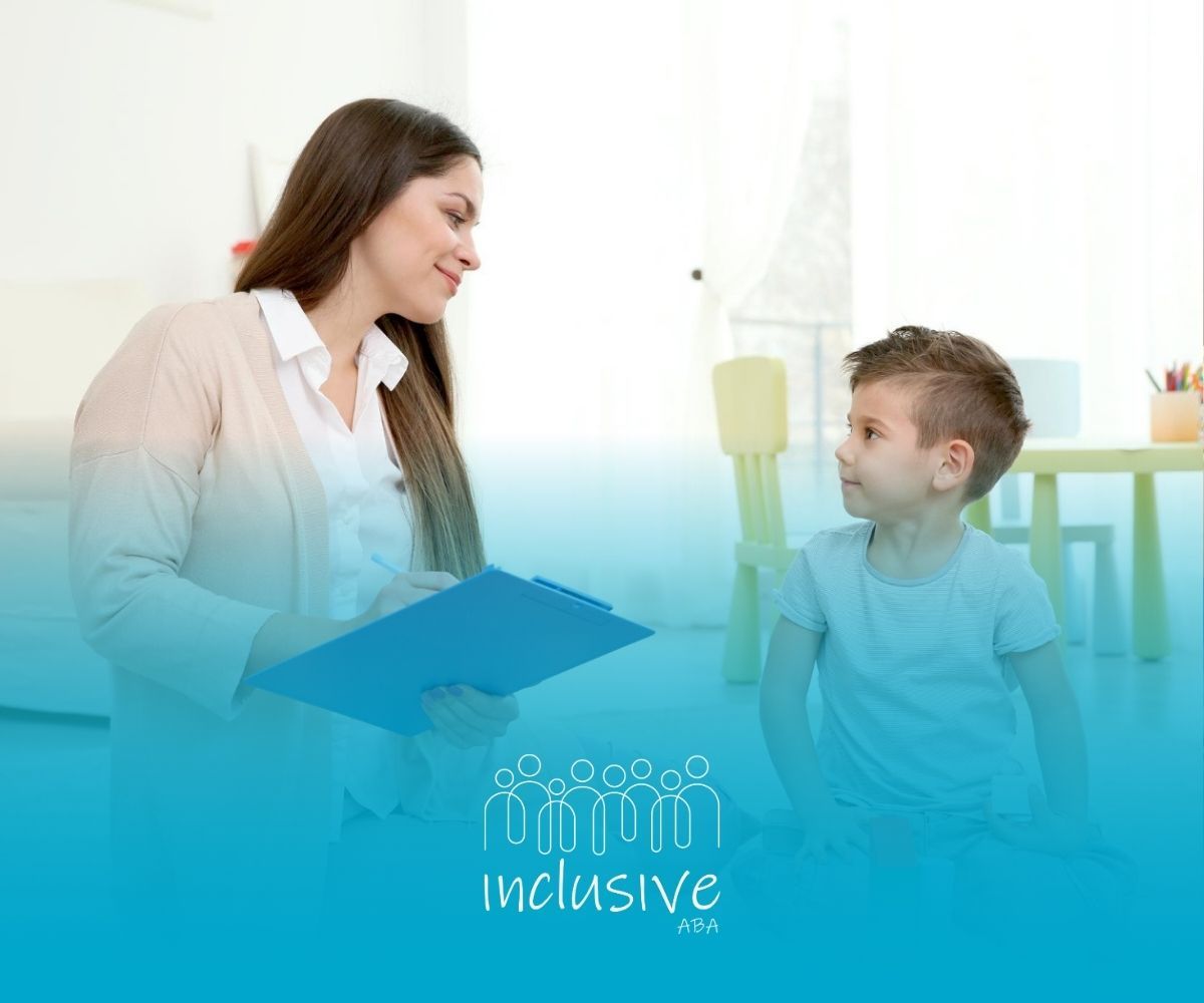 A BCBA is sitting on the floor talking to a young boy who is playing with blocks.