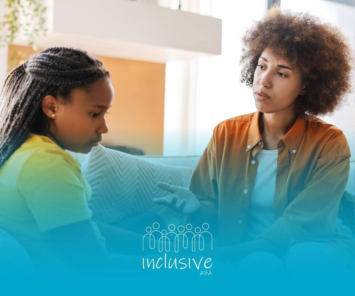 An ABA therapist is sitting on a couch talking to a young girl in ABA therapy.
