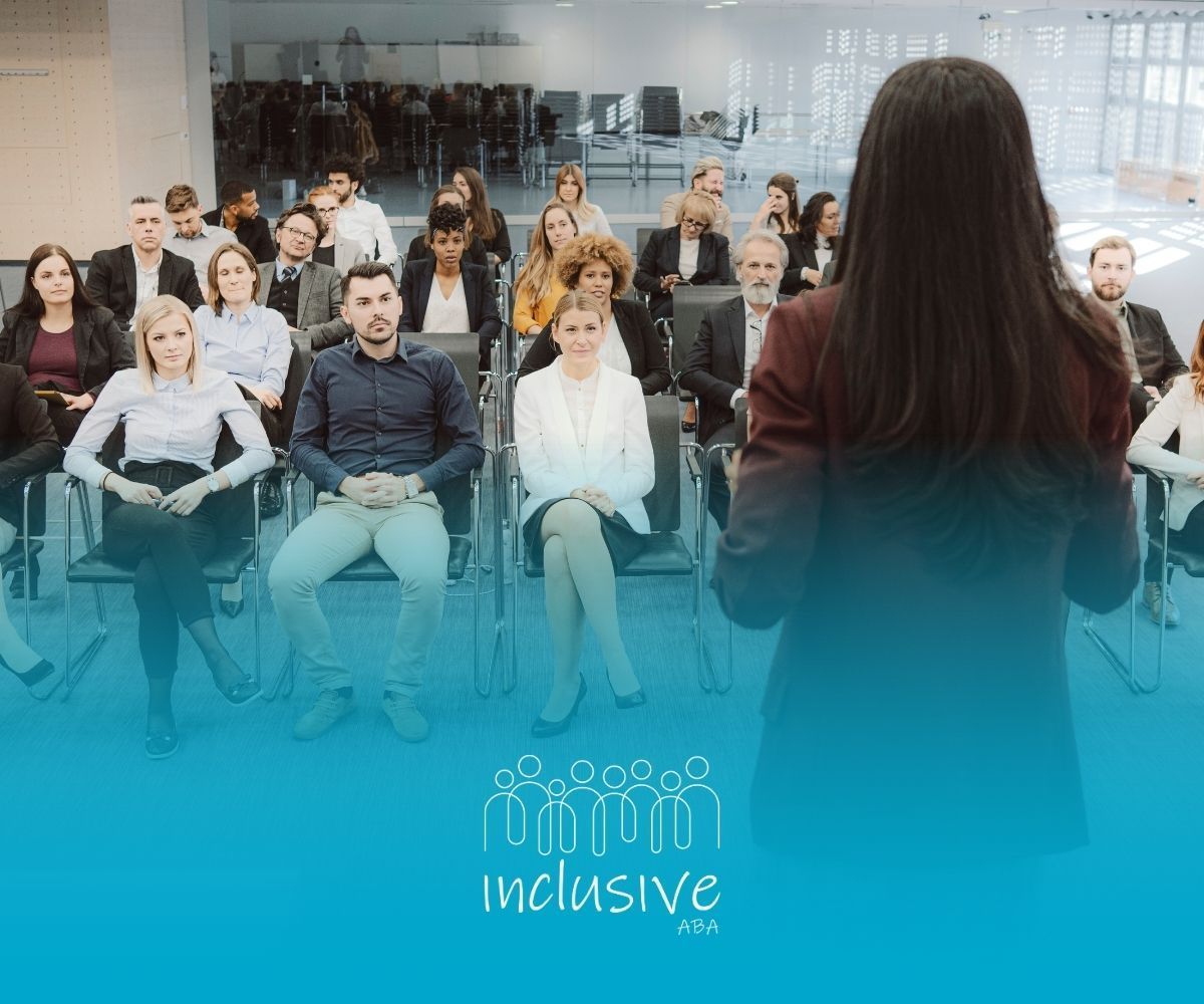 Woman speaking to seated audience at a conference. Teal color at the bottom, “inclusive” logo.