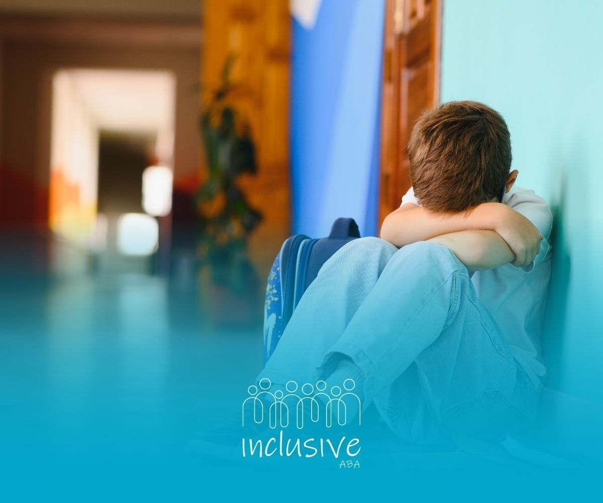 Boy in light blue clothing sits against a wall, head down, appearing distressed.