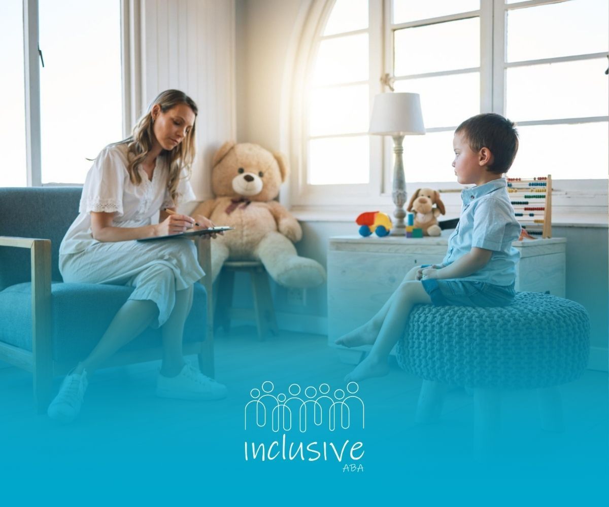 A BCBA is sitting in a chair talking to a young boy.