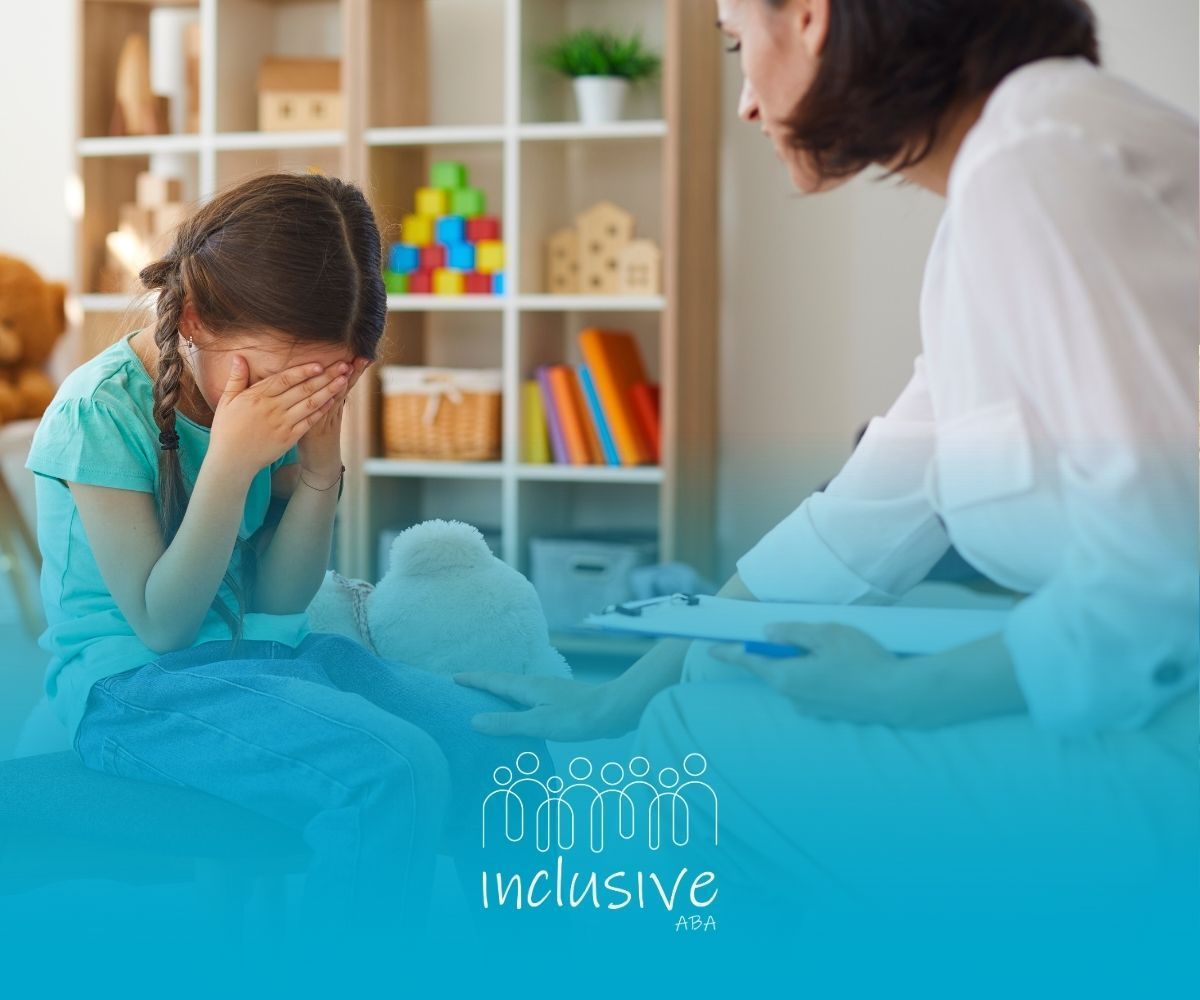 A young girl crying, covering her face, sits with a counselor in a therapy room.