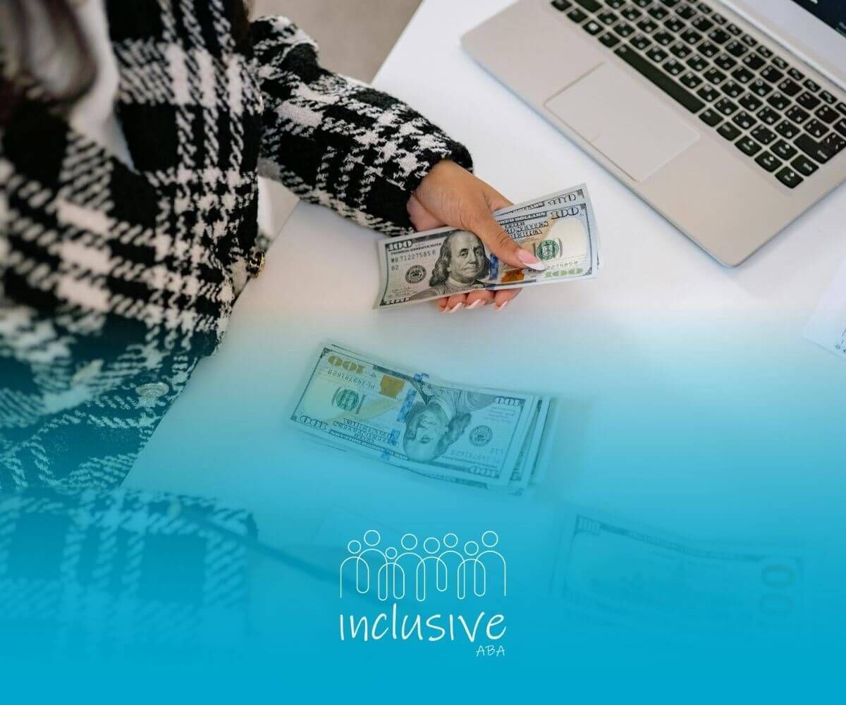 RBT counts cash & writes notes beside an open laptop on a desk, focused on budgeting or planning.