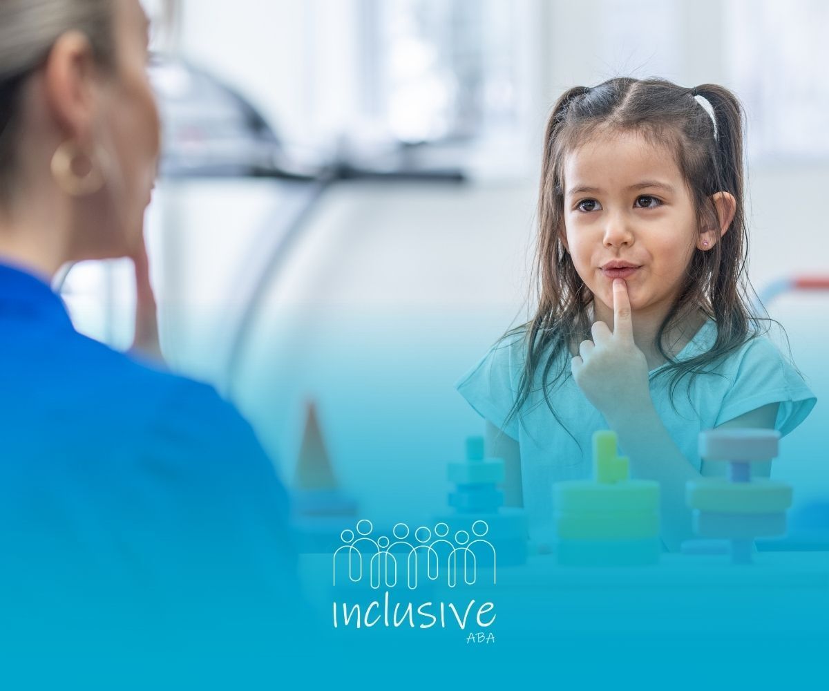 Girl at table with therapist, finger to lips, looking at therapist. Toys on table.