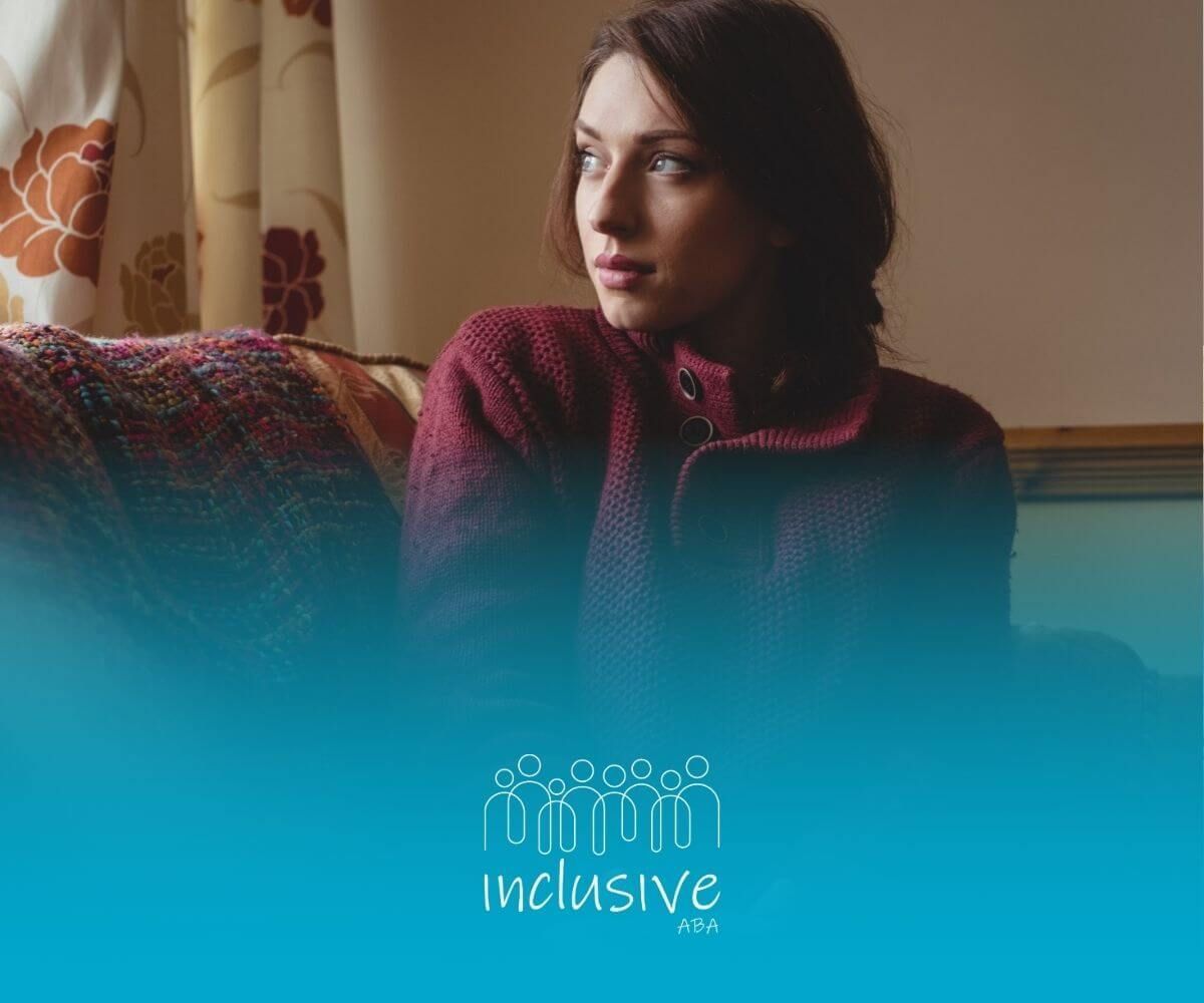 A woman with borderline autism is sitting on a couch wearing a maroon sweater.