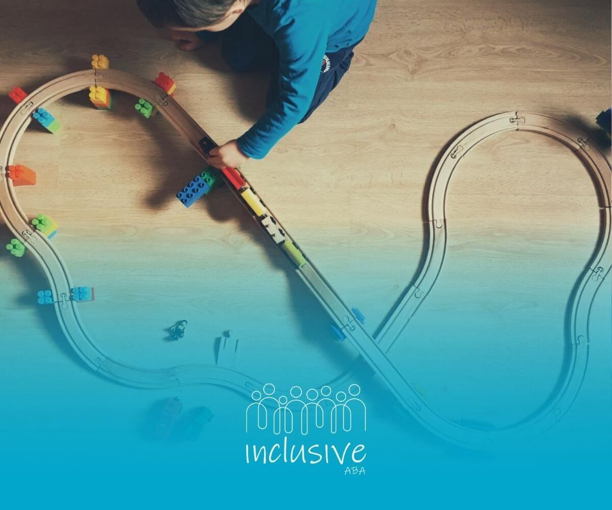 A child with autism is playing with a wooden train set on the floor in ABA therapy.