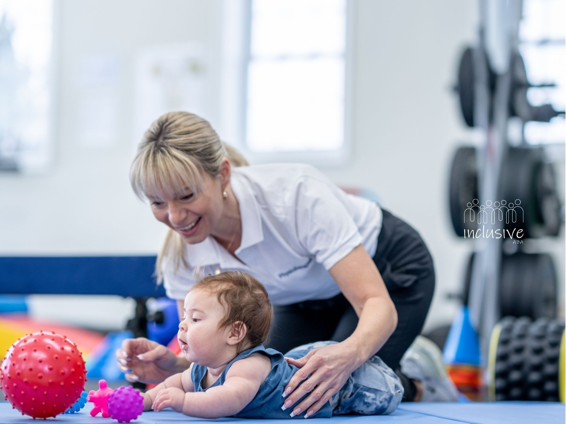 A woman is playing with a baby on the floor in a gym.