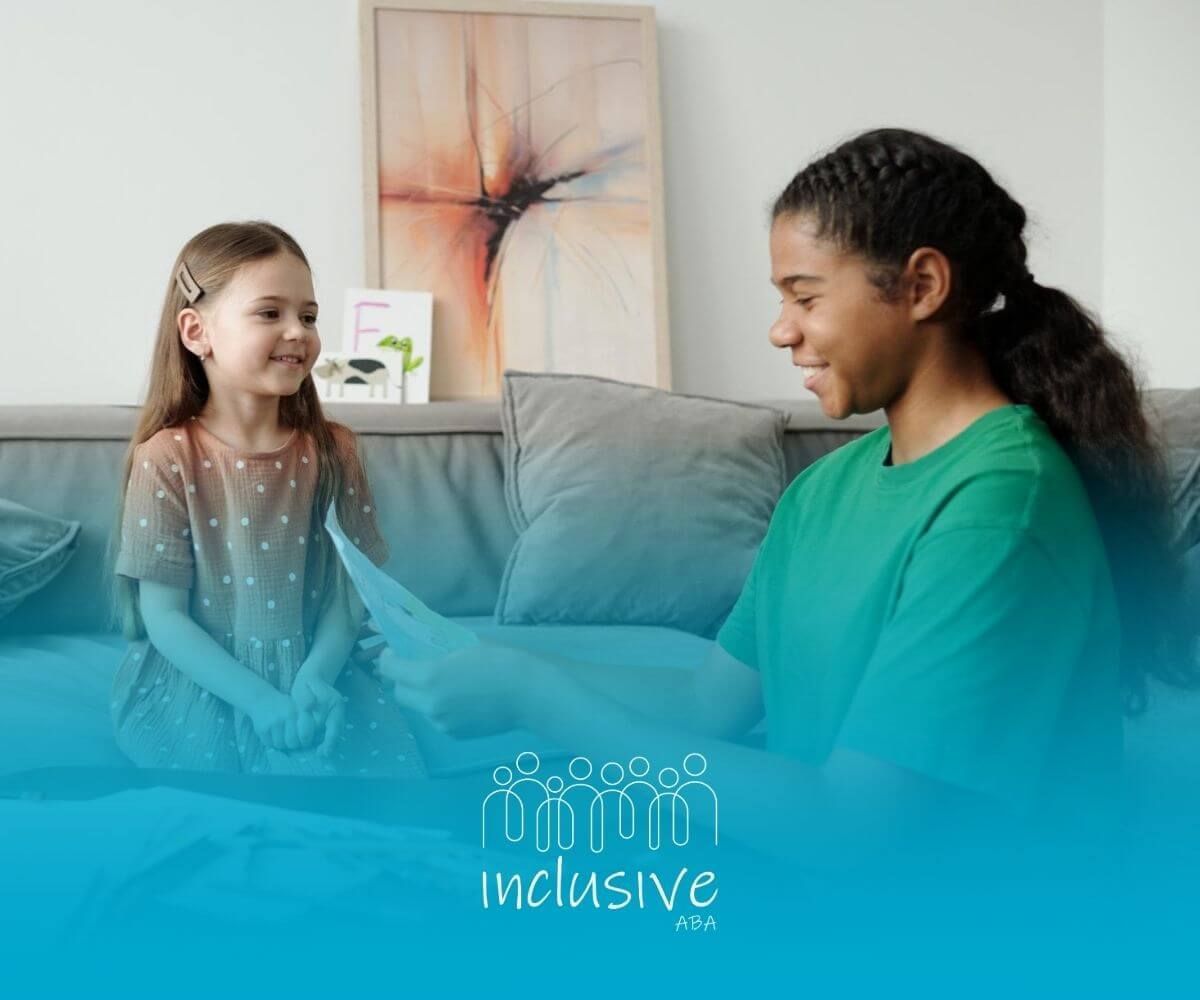 A BCBA and child with autism sitting on a couch, one smiling and handing a drawing to the other.