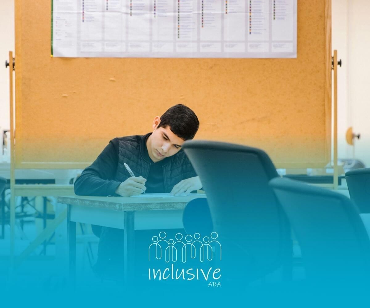 BCBA student leans forward at a desk, focused on writing in a quiet, empty classroom setting.