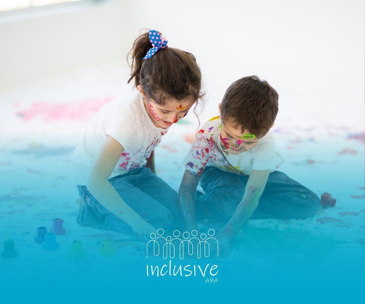 A boy and a girl are sitting on the floor covered in paint.