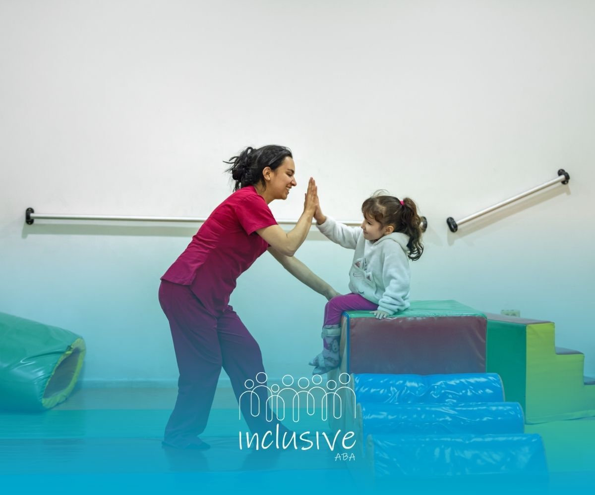 Two children high-five on a padded step in a therapy room with handrails and a blue mat.