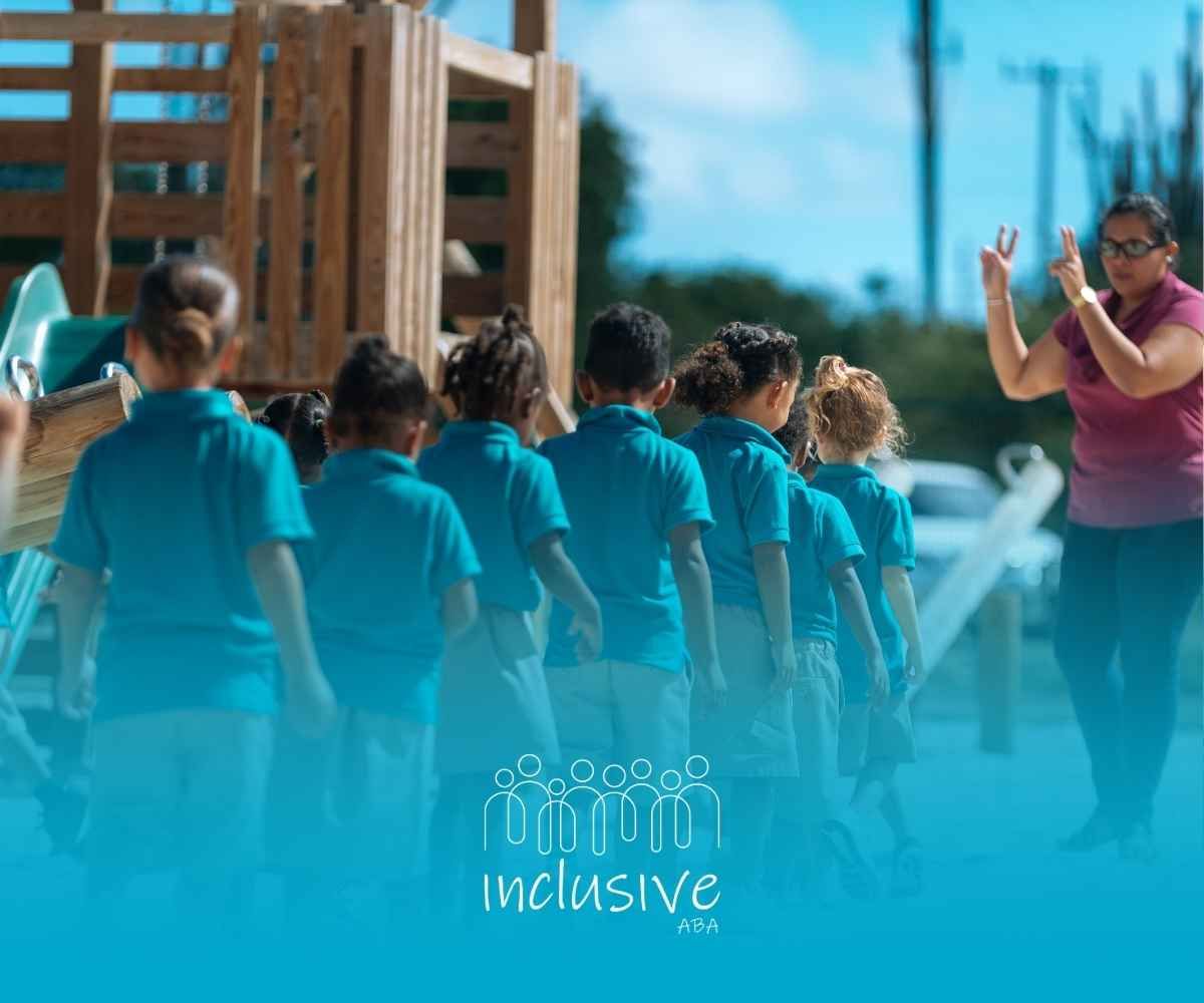 A teacher in a pink shirt counts children in blue shirts lined up on a playground.