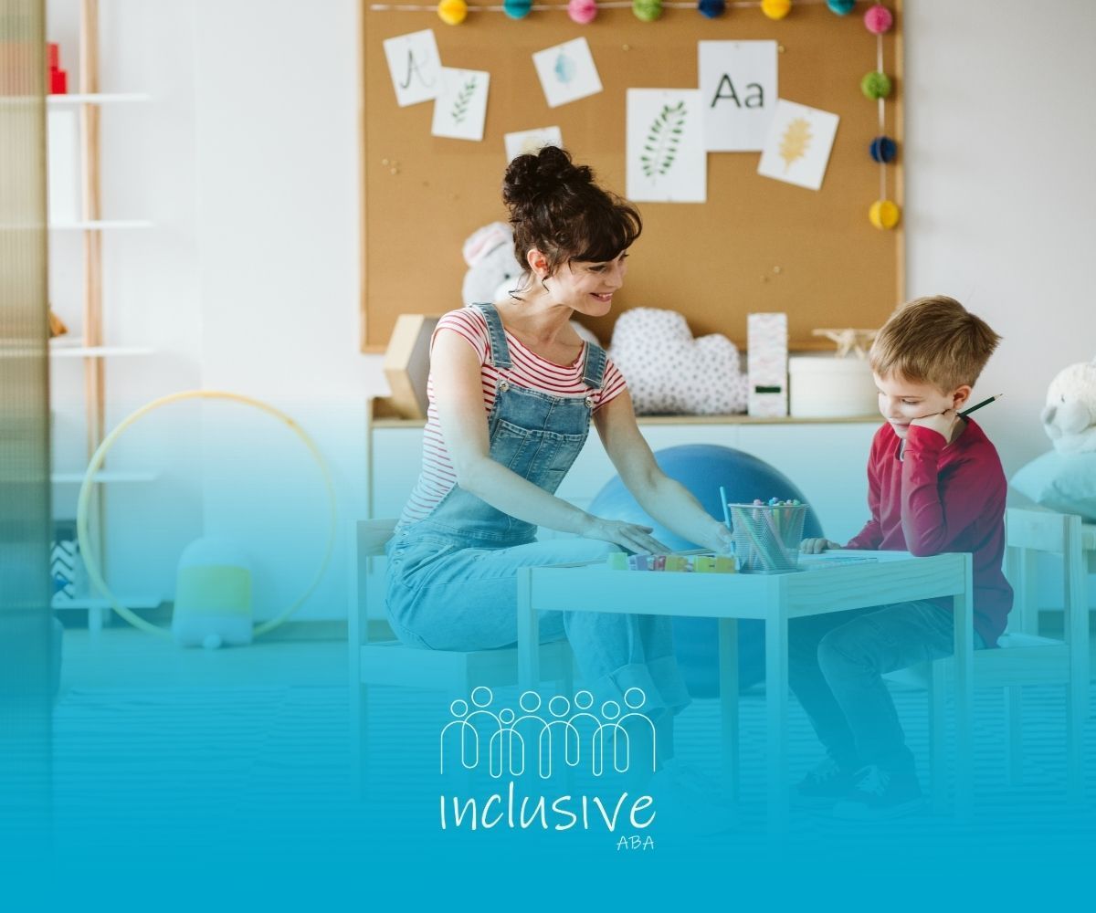 An adult sits at a table with a child in a classroom, working together on a task with art supplies.