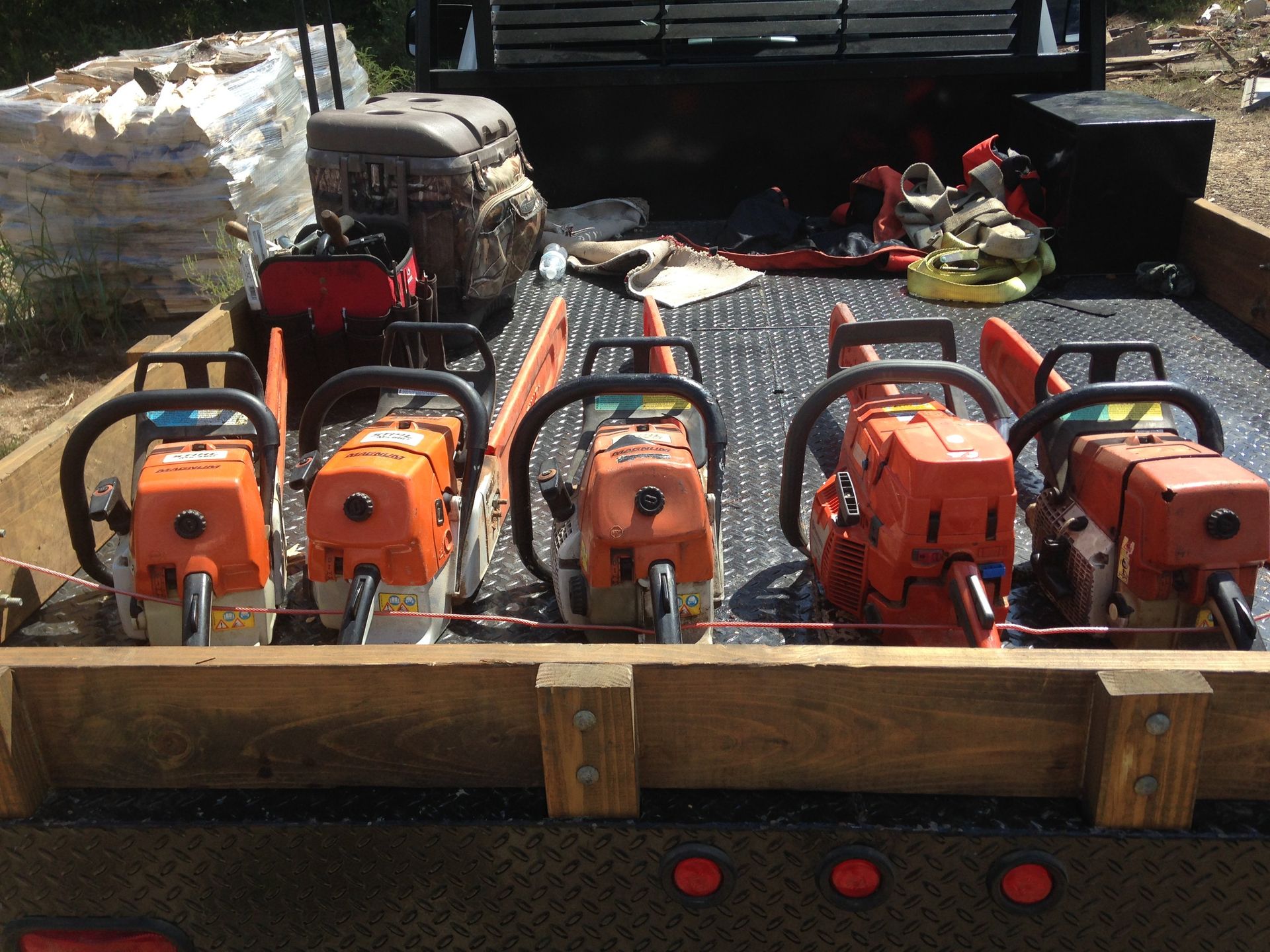 Five orange chainsaws secured in a wooden bed of a truck, ready for use.