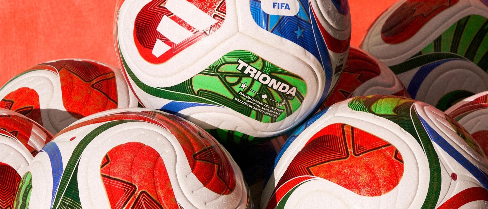Soccer balls stacked, featuring red, white, blue, and green designs. 