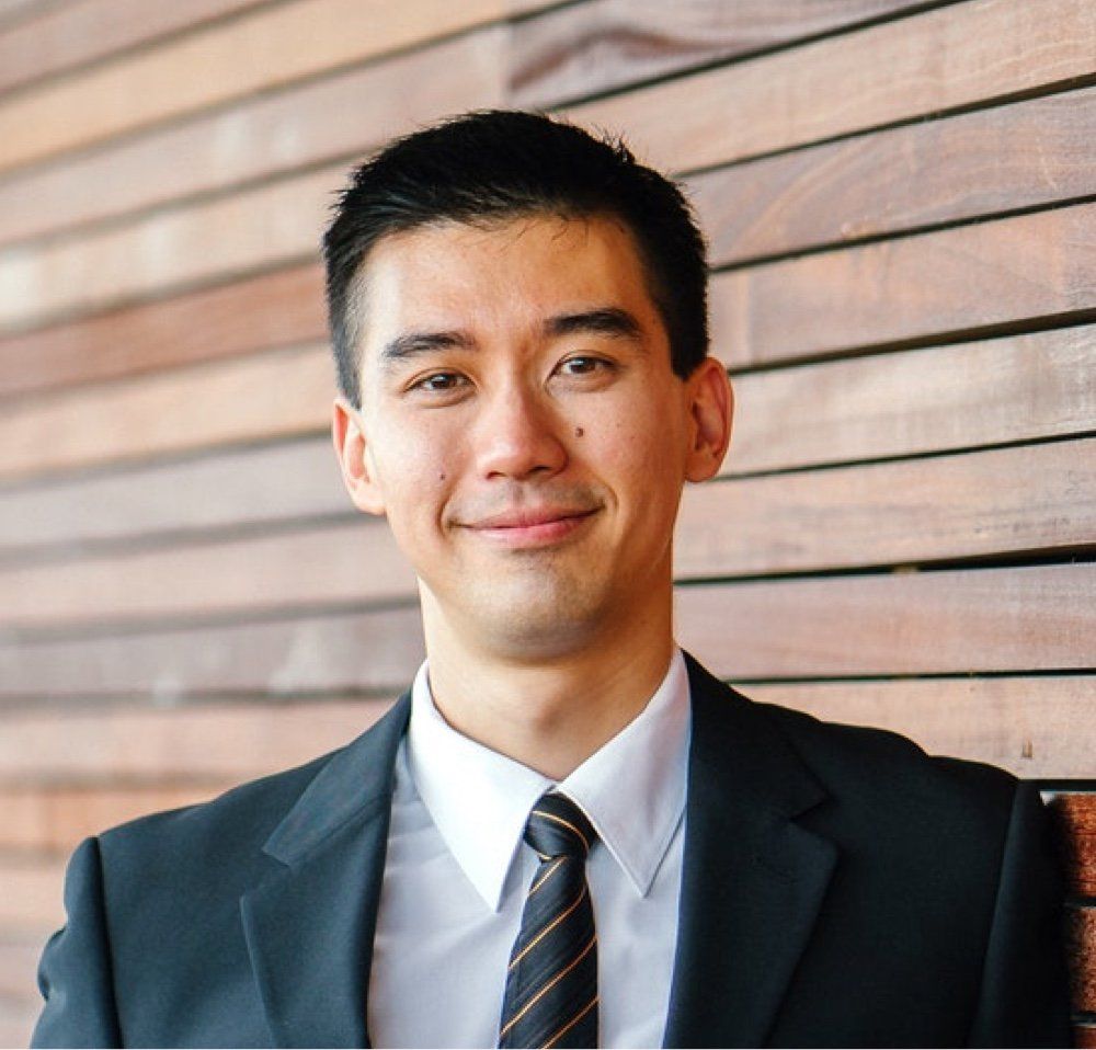 A man in a suit and tie is smiling in front of a wooden wall