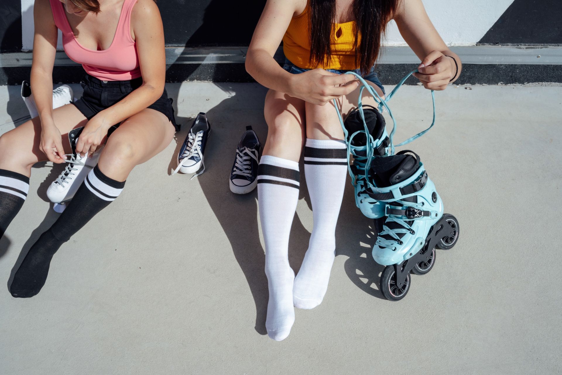 Two women are sitting on the ground tying their roller skates. Two women are sitting on the ground tying their roller skates.