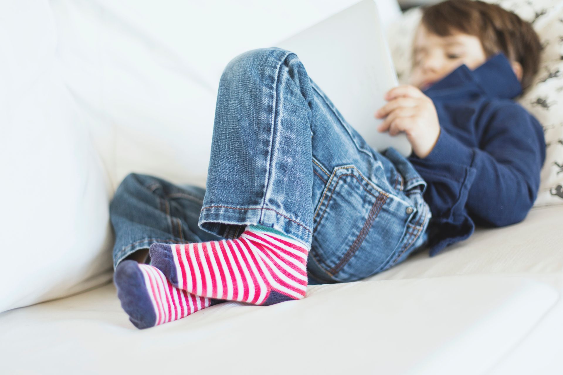 A young boy is lying on a couch using a tablet computer. A young boy is lying on a couch using a tablet computer.