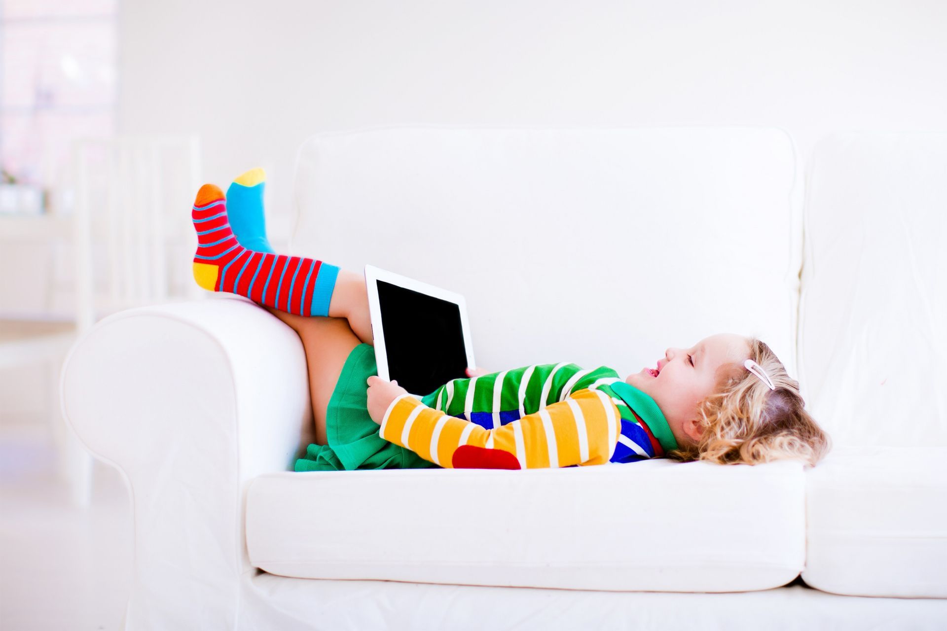 A little girl is lying down on a couch using a tablet computer. A little girl is lying down on a couch using a tablet computer.
